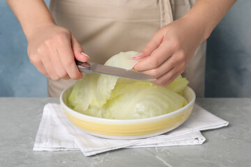 Woman preparing stuffed cabbage rolls at light grey table, closeup