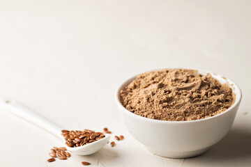 Flaxseed flour in a bowl and flax seeds on a light background. Selective focus. Close-up, copy space