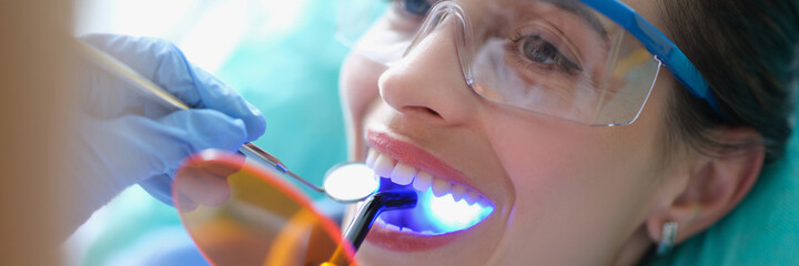 Woman in safety glasses undergoing treatment at dentist using light lamp