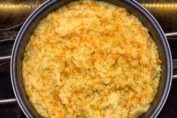 Top view of traditional Italian yellow risotto, closed view forming texture with rice grains, carrot, tomato, onion and green onion.