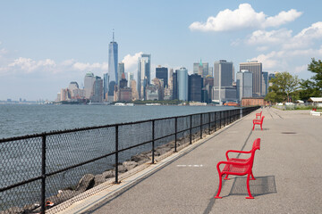 Red Benches along the Shore of Governors Island with a view of the Lower Manhattan Skyline New York City - obrazy, fototapety, plakaty