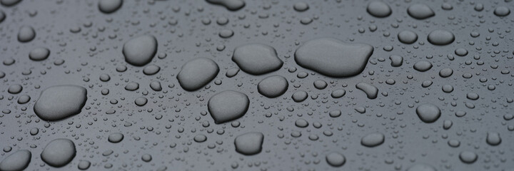 Closeup of raindrops on black hood of car background