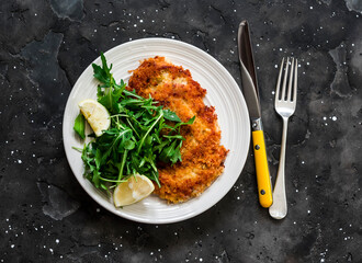 Garlicky bread crumbs crispy turkey schnitzel and fresh lemon arugula salad on a dark background,...