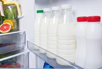 against the background of a white open refrigerator, bottles with milk in the door on the shelf