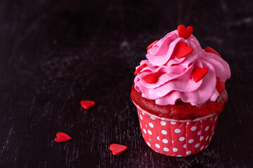 Valentine's day cupcake is decorated with red hearts on black background. Copy space. Delicious delicacy. Muffin with cream. Cake. low key