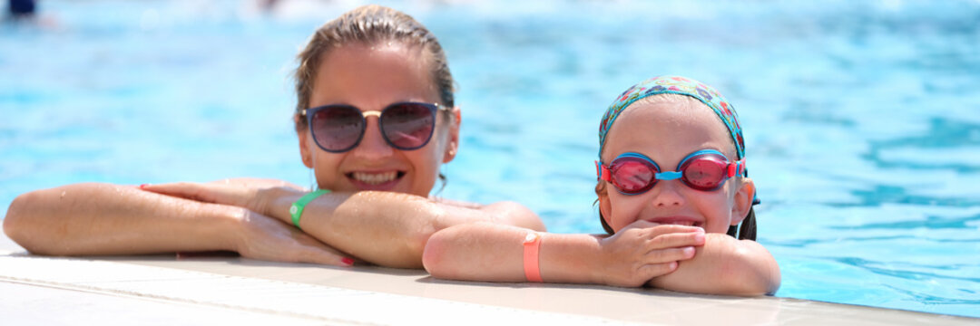 Little girl in swimming goggles and mother lying on side of pool