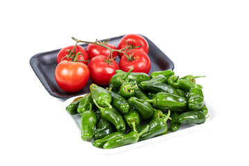 Red vine tomatoes on a black tray and green peppers on a white tray on a white background