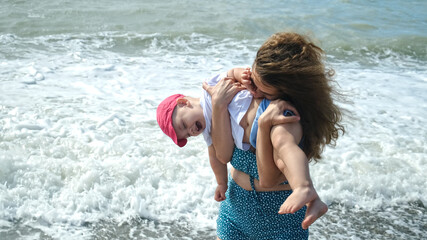 Family sea resort. Young mother tickles her little son, ocean on background. Baby laughs in mother's arms. Son and mom having fun together. Happy family vacation. 