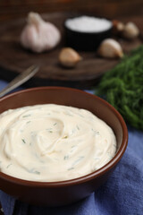 Tasty creamy dill sauce in bowl on blue kitchen towel, closeup