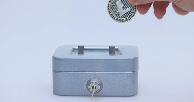 Male hand puts a cryptocoin, Litecoin or LTC, in a small grey vault, safe or piggy bank, depicting crypto or cryptocurrency saving, holding or hodling. High quality 4k footage