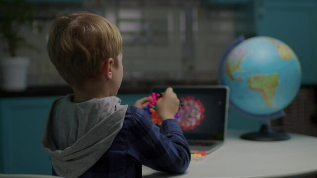 School boy playing color toys making model of virus sitting at home. Kid using tablet computer for modeling virus with toys.