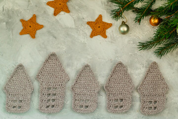 Christmas concept. Crocheted white, gingerbread house, yellow stars and fir tree branches on a background.