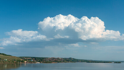 group of white cumulus clouds on blue sky over hilly river bank as natural background
