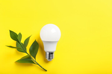 Light bulb and branch with green leaves on yellow background, flat lay. Space for text