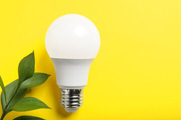 Light bulb and branch with green leaves on yellow background, flat lay. Space for text