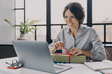 Happy cheerful Italian woman home office worker sits at desk unpacks newly received New Year gift