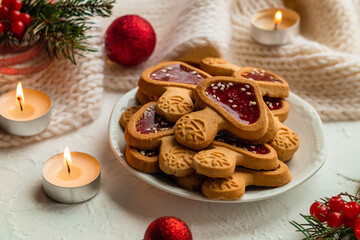 Christmas cookies on a white plate among small candles, spruce branches and red balls.