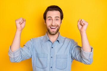 Fototapeta premium Photo portrait of young man smiling gesturing like winner wearing denim shirt isolated on bright yellow color background