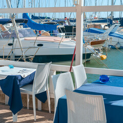 Obraz premium A fragment of a coastal cafe on the Black Sea embankment against the backdrop of moored modern boats and yachts. Sochi. Russia