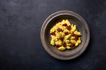Traditional Italian potato gnocchi with parmesan and dried tomatoes in rustic plate on a graphite dark background. Top view