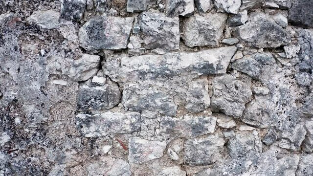 Old stone wall - rough texture of aged vintage ruin of an ancient historical building at archaeological site. Detail closeup of grey medieval structure.