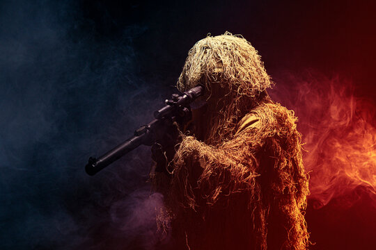 A member of a special purpose unit. Russian special forces soldiers with a silent sniper rifle in camouflage in clouds of smoke on a black background with colored illumination.
