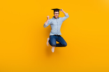 Full length photo of young man happy positive smile jump up rejoice master degree college hat isolated over yellow color background - obrazy, fototapety, plakaty