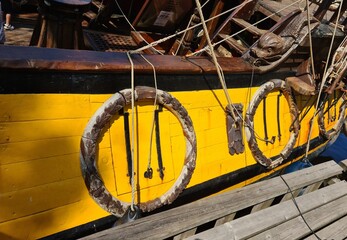 Closed cannon ports on the wooden side of an old sailing ship docked at the pier © Anatolijs