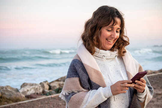 Happy baby  boomer woman with a blanket on the beach looking at her mobile phone