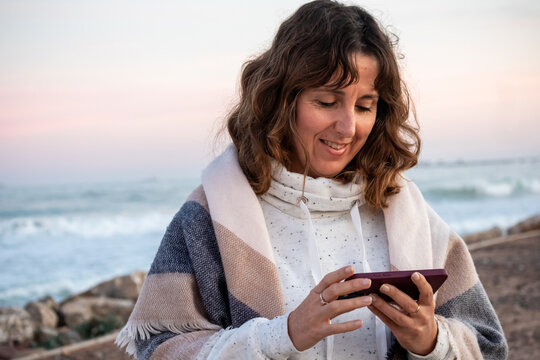 Baby boomer woman in winter on the beach looking at her mobile phone
