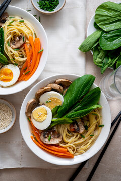 Two bowls with vegan soup with noodles, vegetable broth, mushrooms, eggs, carrots. Top view, assian food.