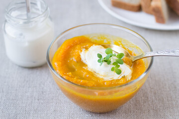 Pumpkin cream soup in a glass bowl and sour cream