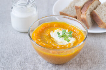 Pumpkin cream soup in a glass bowl and sour cream