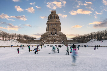 People playing ice hockey and skating on ice in front of the Monument to the Battle of the Nations...