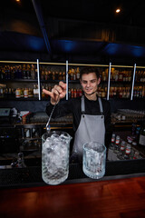 Barman stirring ice cubes in cocktail glass with spoon