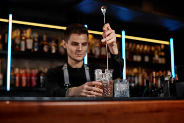 Barman stirring ice cubes in cocktail glass with spoon