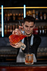 barman in apron pours old fashioned cocktail into glass