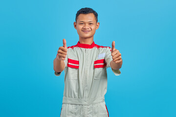 Portrait of smiling young Asian mechanic showing thumb up gesture isolated on blue background