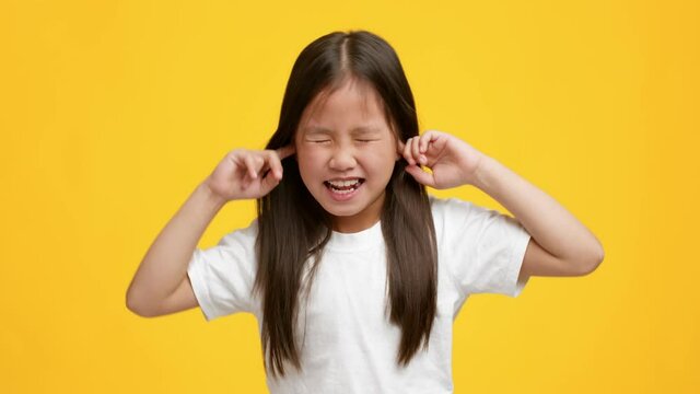 Naughty Little Asian Girl Plugging Ears With Fingers, Yellow Background