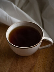 Breakfast in bed, a cup of black tea and thin pancakes with currant jam and sour cream on a beige ceramic plate on a wooden tray on a soft white bed in the morning light