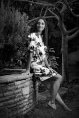 Black and white image of a young woman in flower print dress, exploring a woodland garden.
