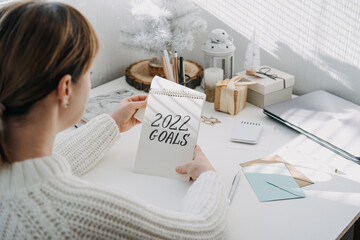 2022 goals, New year resolution. Woman in white sweater writing Text 2022 goals in open notepad on...
