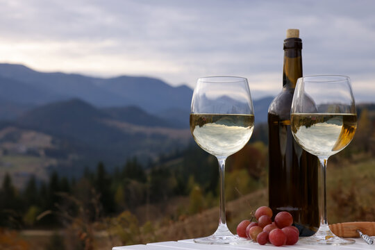 Tasty wine and fresh grapes on white wooden table against mountain landscape. Space for text
