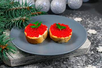 Sandwiches with red caviar on a gray plate on a stone table against the background of a Christmas tree and Christmas balls. Christmas, New Years holidays. Festive food.