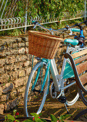 Fototapeta na wymiar Retro bicycle with braided willow basket by stone wall with wooden bench at street.