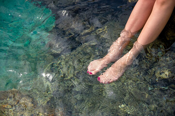 Kobiece nogi z pomalowanymi paznokciami zanurzone w przejrzystej lazurowej wodzie - obrazy, fototapety, plakaty
