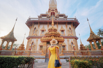 Travel by Asia. Young woman in hat and yellow dress walking near the Chalong buddhist temple on Phuket Island in Thailand.