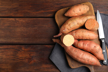 Whole and cut ripe sweet potatoes on wooden table, flat lay. Space for text