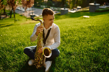 Young saxophonist with saxophone sitting on grass
