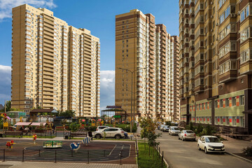 Fototapeta na wymiar Three tall apartment buildings next to a playground and a blue sky. A new residential area of a developing city. Yellow multistory with balconies.